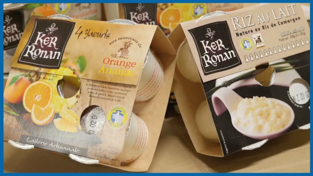 Deux boîtes de quatre yaourts Ker Ronan posées sur une table, dont un pack de yaourts saveur orange-ananas et un pack de riz au lait, avec les emballages bien visibles à l’avant.