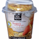 Quatre pots de snacking lacté Ker Ronan à la fraise posés sur un fond blanc, avec un petit gâteau breton placé au-dessus.